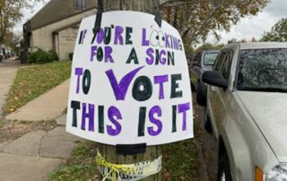 Sign with black and purple letters that reads "If you're looking for a sign to vote this is it"