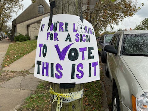 Sign with black and purple letters that reads "If you're looking for a sign to vote this is it"